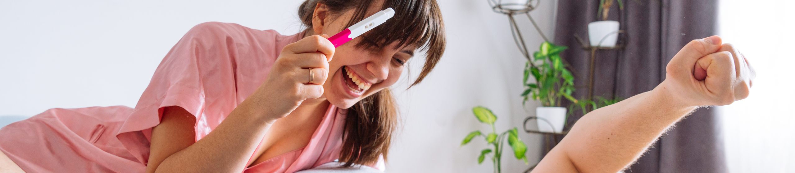 Щастлива двойка в леглото. Жена показва на мъжа положителен тест за бременност.