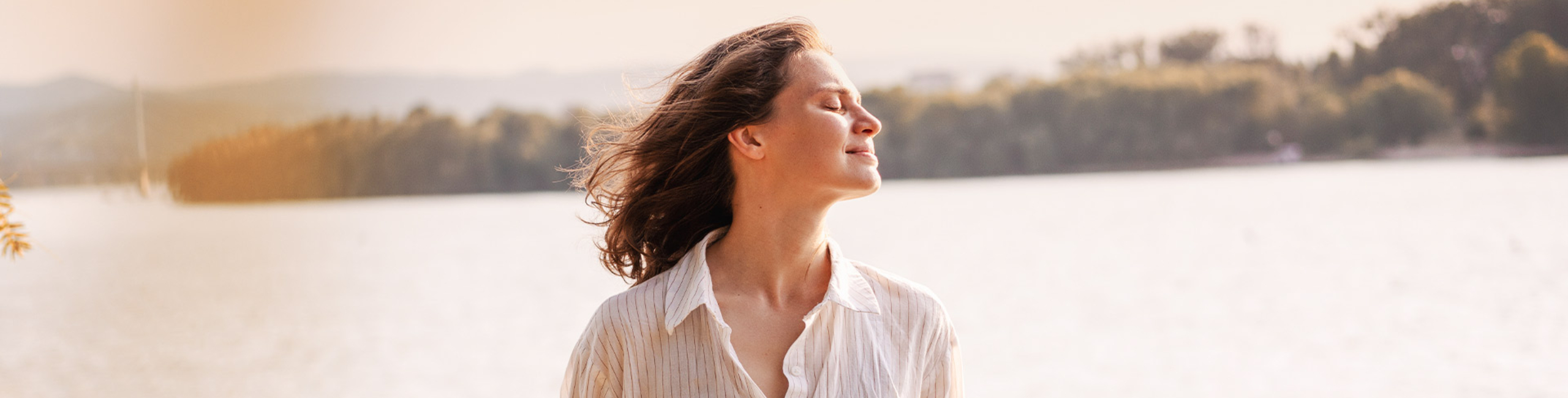 Жена, стояща навън край езеро, се наслаждава на слънцето със затворени очи