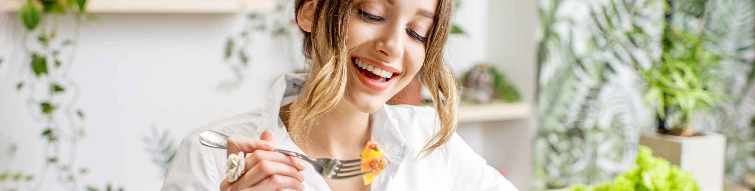 Усмихната жена яде здравословна салата на масата