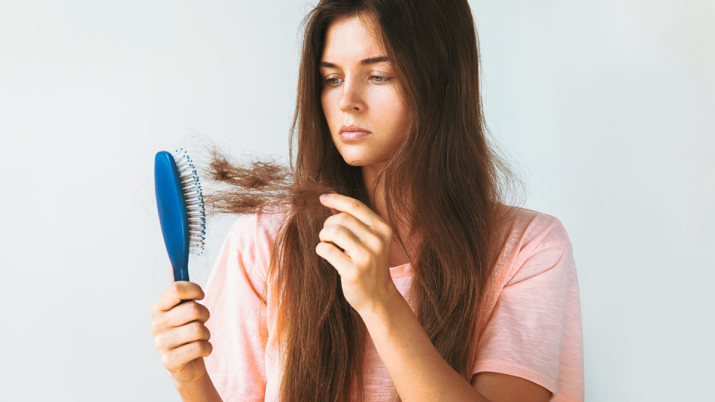 Жена, държаща четка с изскубана коса поради косопад