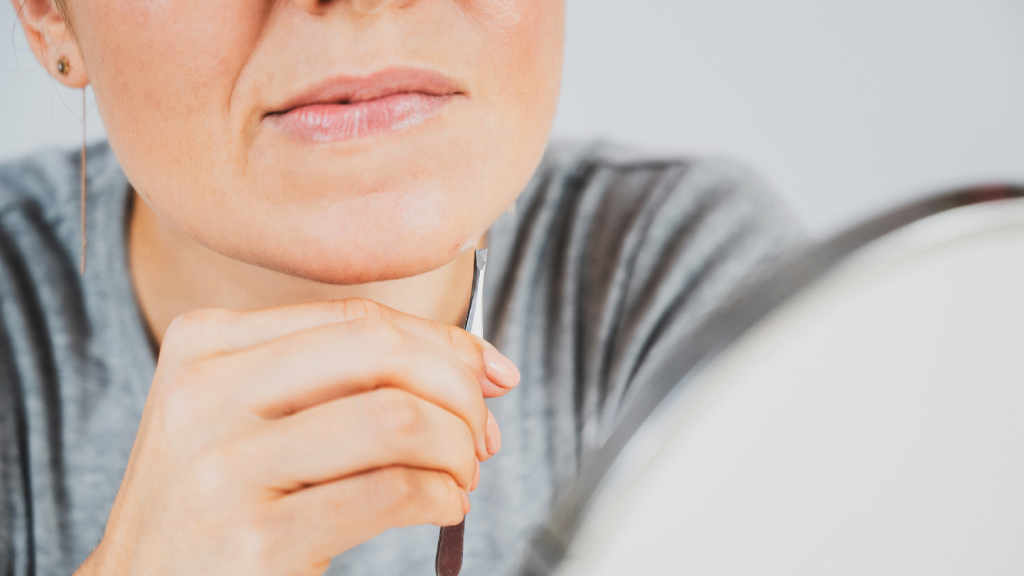 Жена премахва косми от брадичката си с пинсети, отблизо